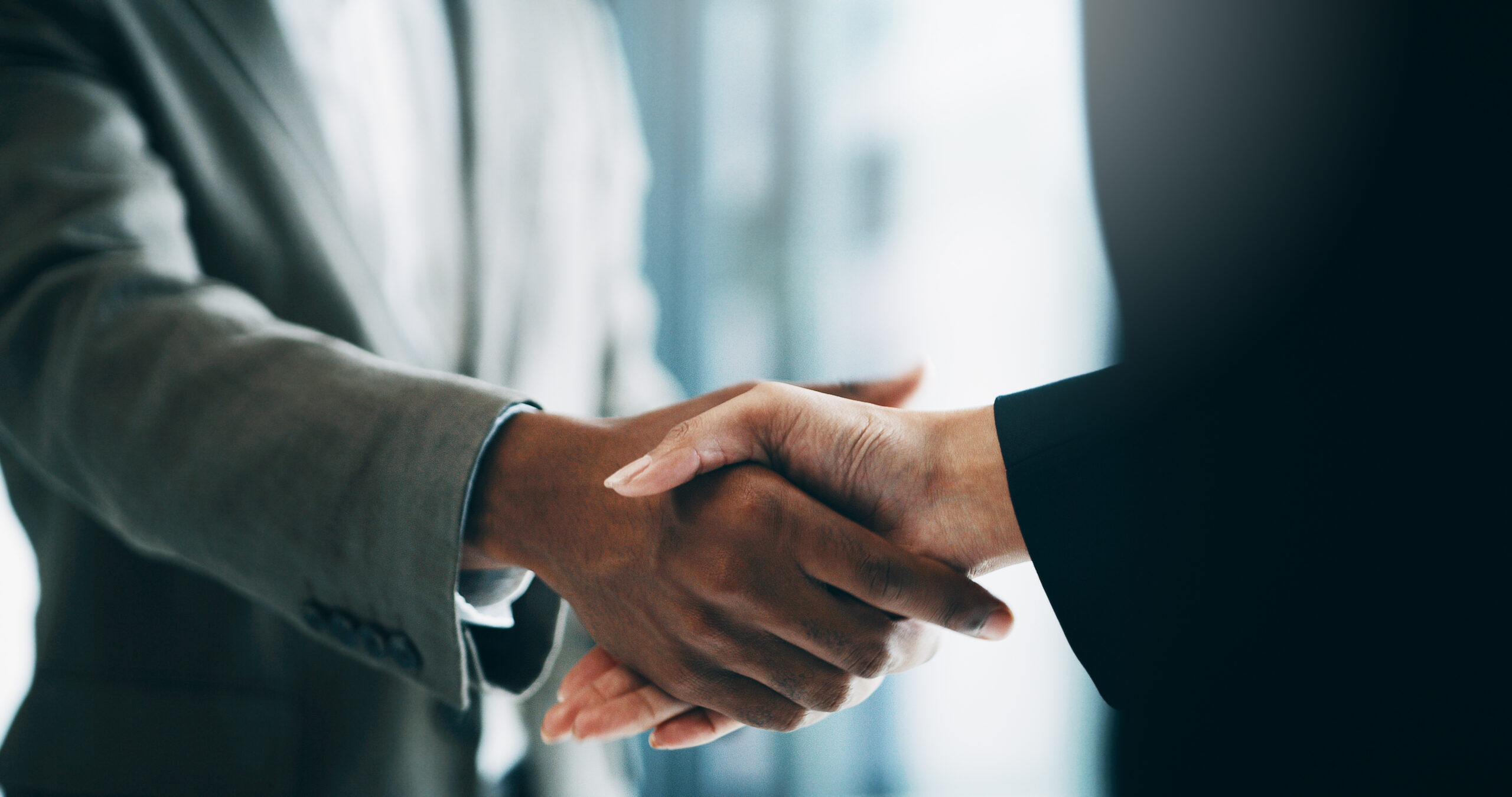 Two business professionals shaking hands in a formal setting, with a focus on their clasped hands.