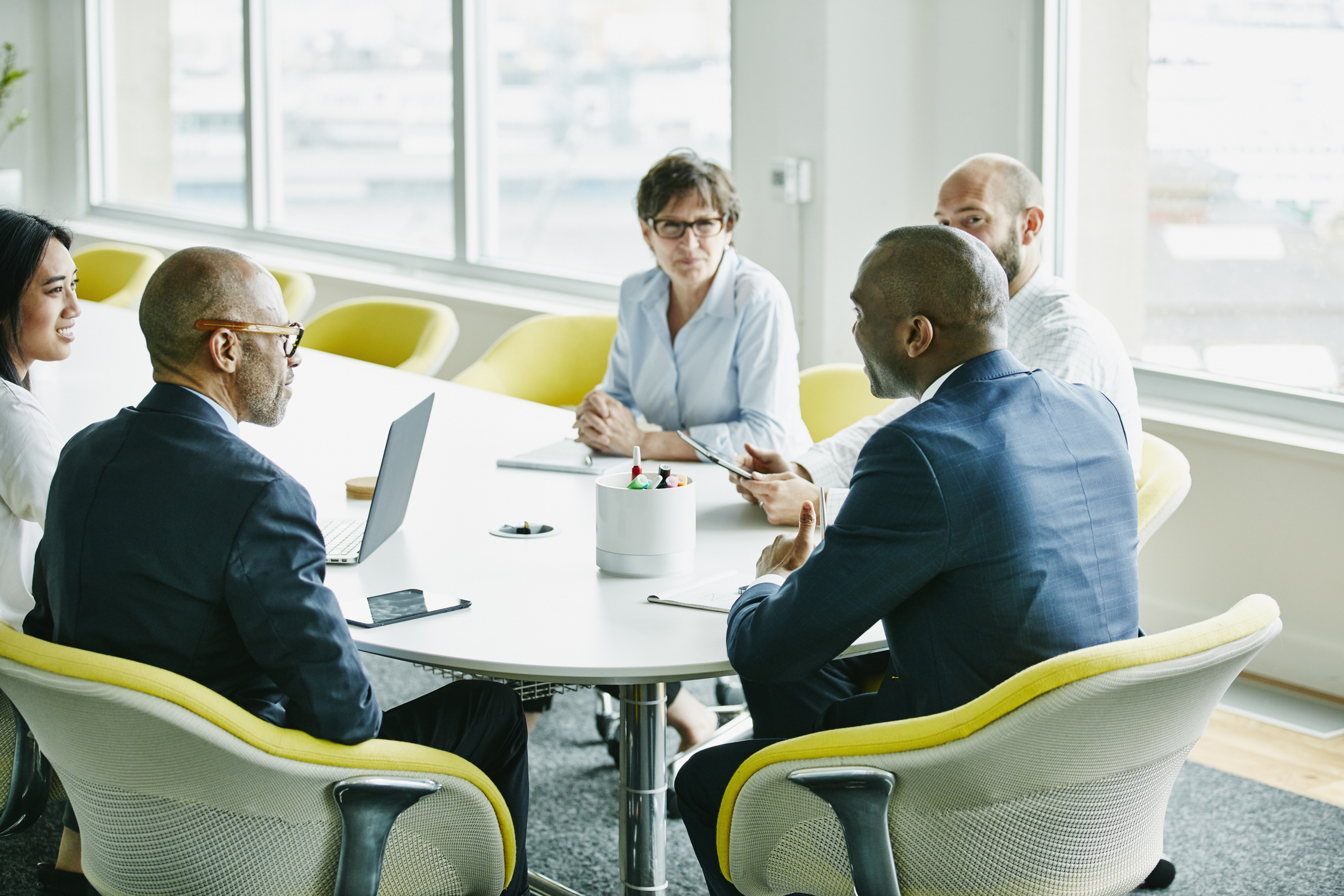 Diverse group of business professionals engaged in a meeting around a table in a bright office setting.